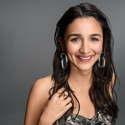 Alia Bhatt wearing AEQEA Weekend Stack Rings and Large Stack Ring with metallic earrings against grey background